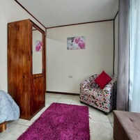 A room with a wooden door, a sofa with a floral pattern, a purple rug, and two wall-mounted pictures of flowers.