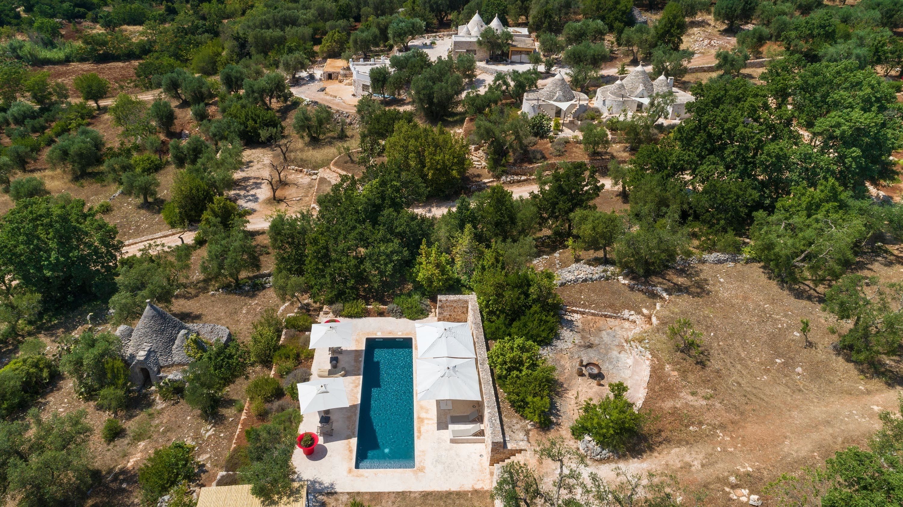 Vista aérea de uma propriedade com piscina, edifícios de pedra e vegetação ao redor.