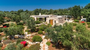 A stone house with a garden, surrounded by trees and vegetation.