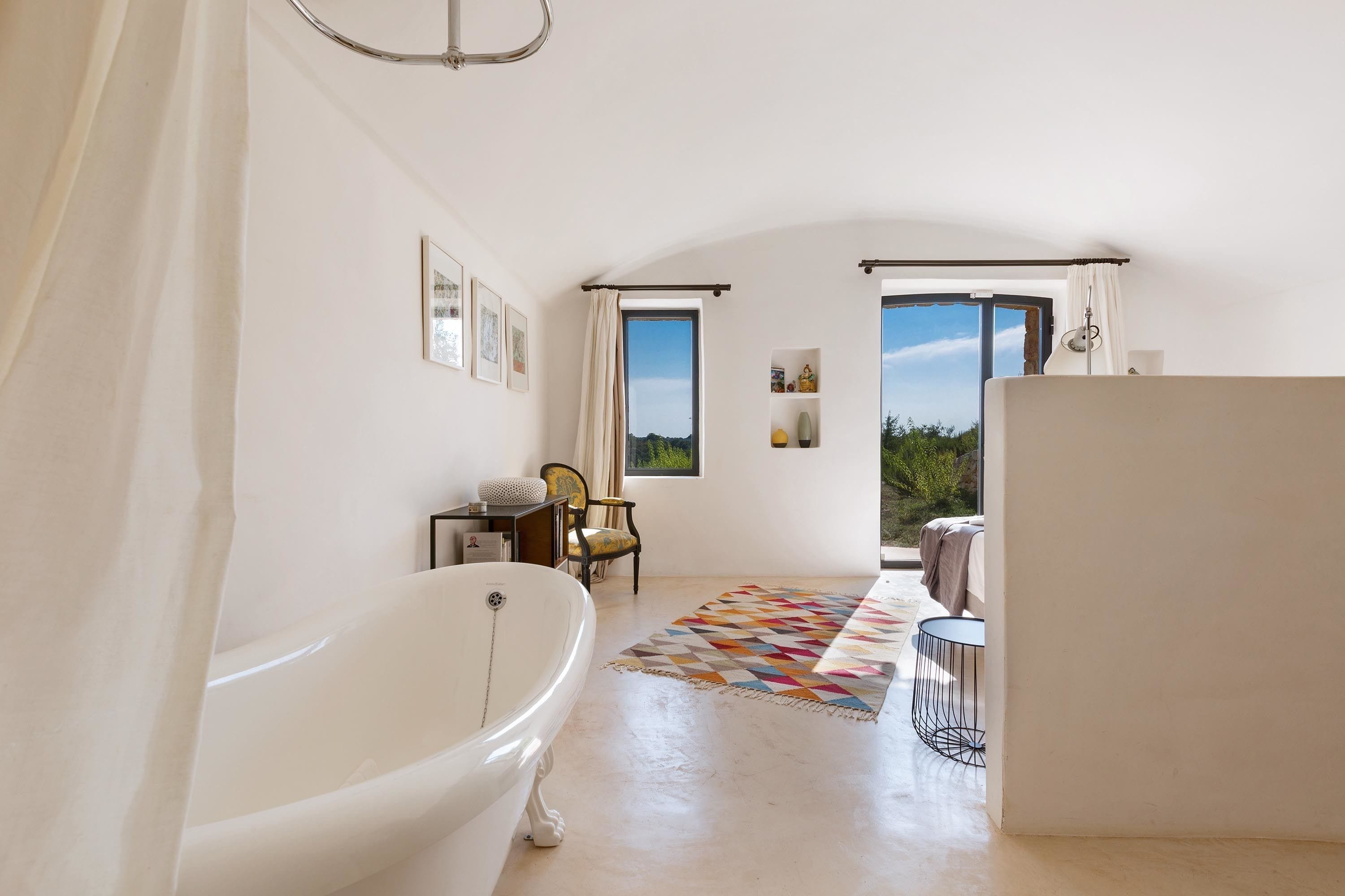 A spacious bathroom with a freestanding bathtub, a window with a view, and a patterned rug on the floor.