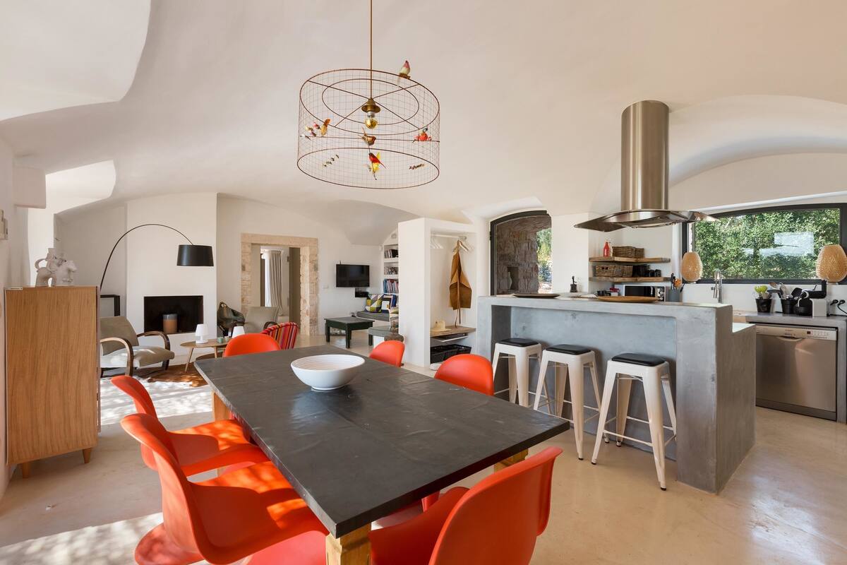 A modern kitchen with a central island, bright orange chairs, and a unique bird-themed pendant light.