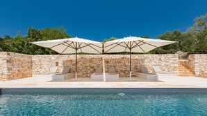 A swimming pool with stone walls and two white umbrellas.