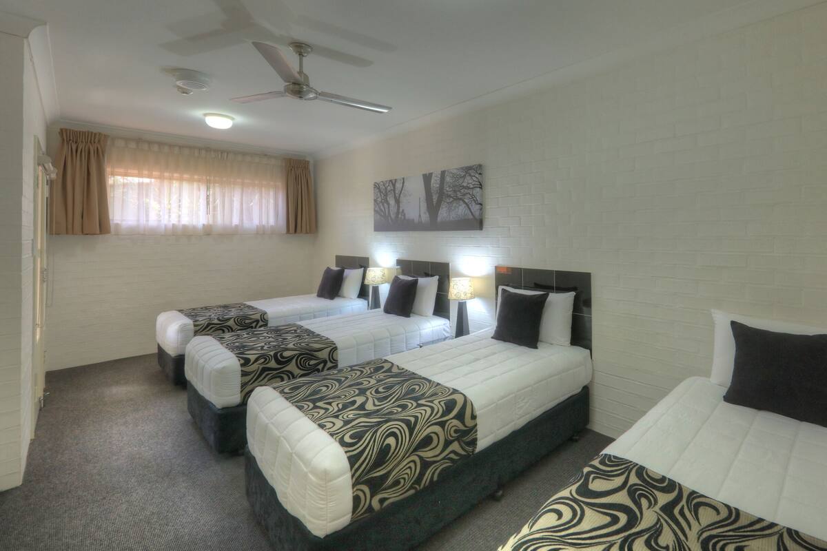 Habitación de hotel con dos camas, un ventilador de techo y una ventana con cortinas.