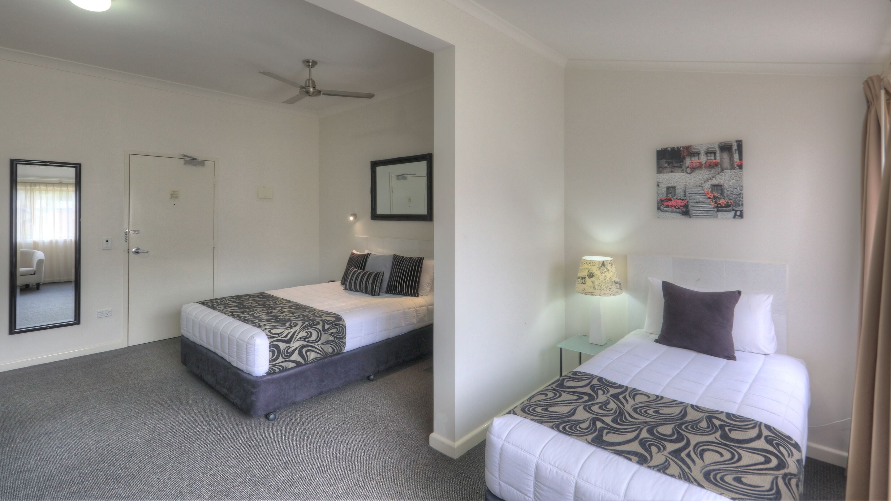 A hotel room with two beds, a ceiling fan, a framed picture, and a lamp.