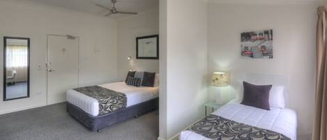 A hotel room with two beds, a ceiling fan, a framed picture, and a lamp.
