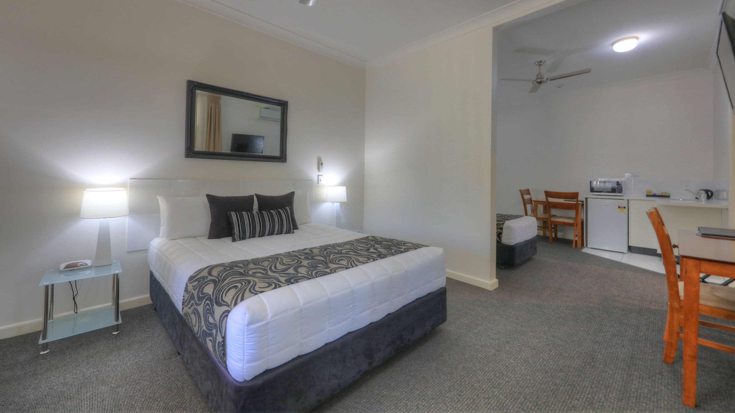 Habitación de hotel con cama, lámparas de noche, escritorio con silla, microondas y un refrigerador pequeño.