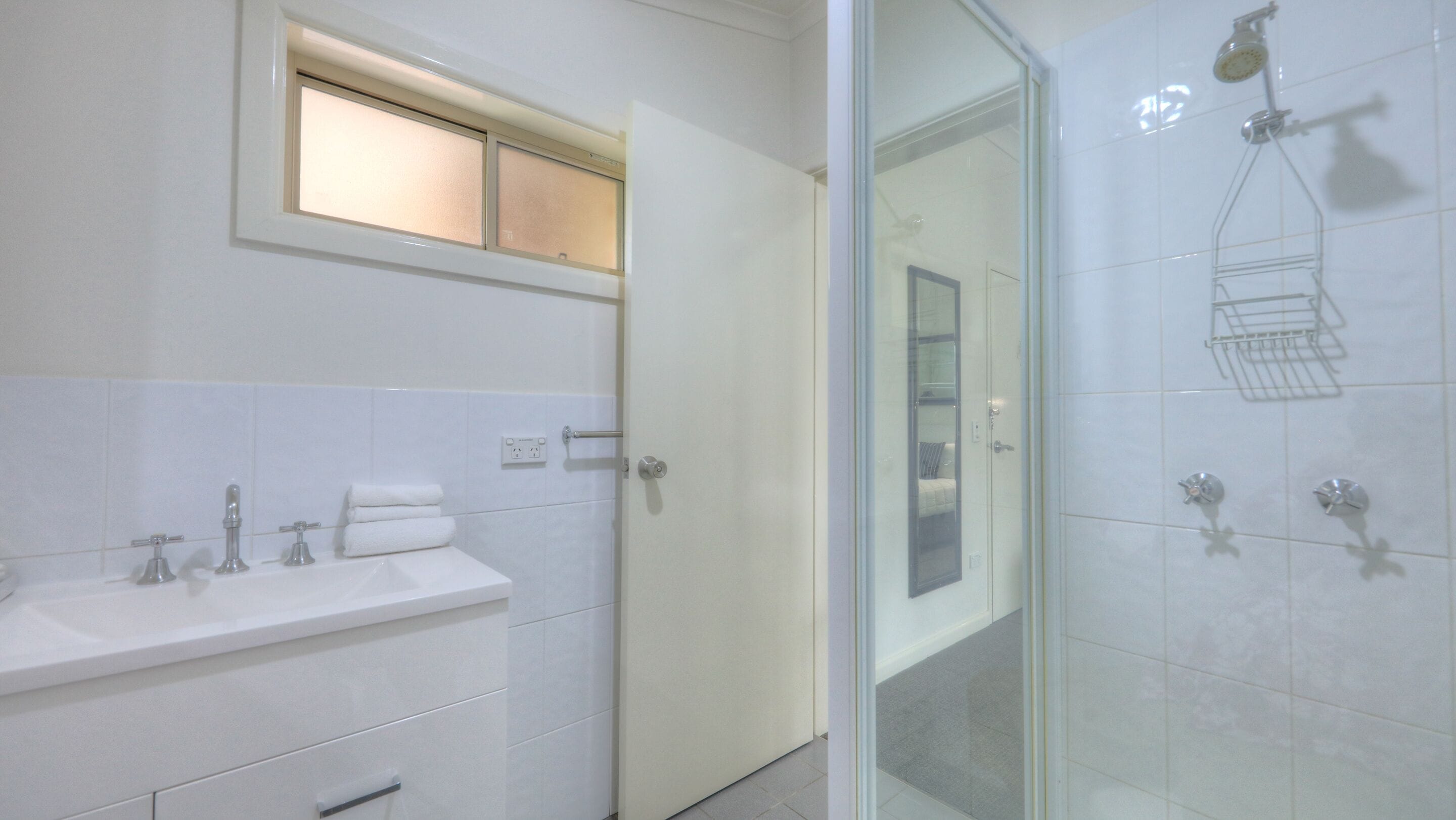 Un baño moderno con cabina de ducha de vidrio, un lavabo con toallero y un pequeño ventanal sobre el espejo.