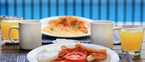 A breakfast setting with toast, eggs, bacon, and tomato on a plate, accompanied by two mugs and glasses of orange juice.