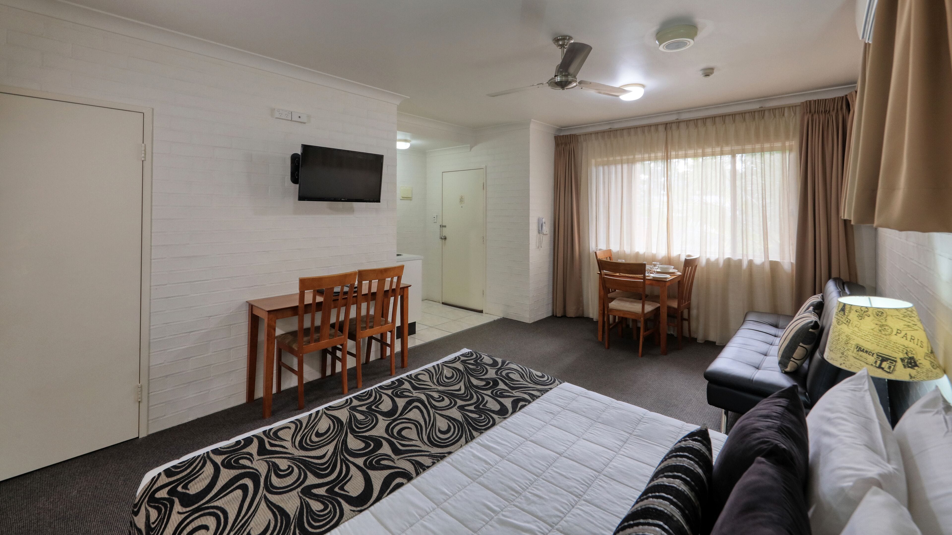 A hotel room with a bed, a desk with chairs, a television, and a window with curtains.