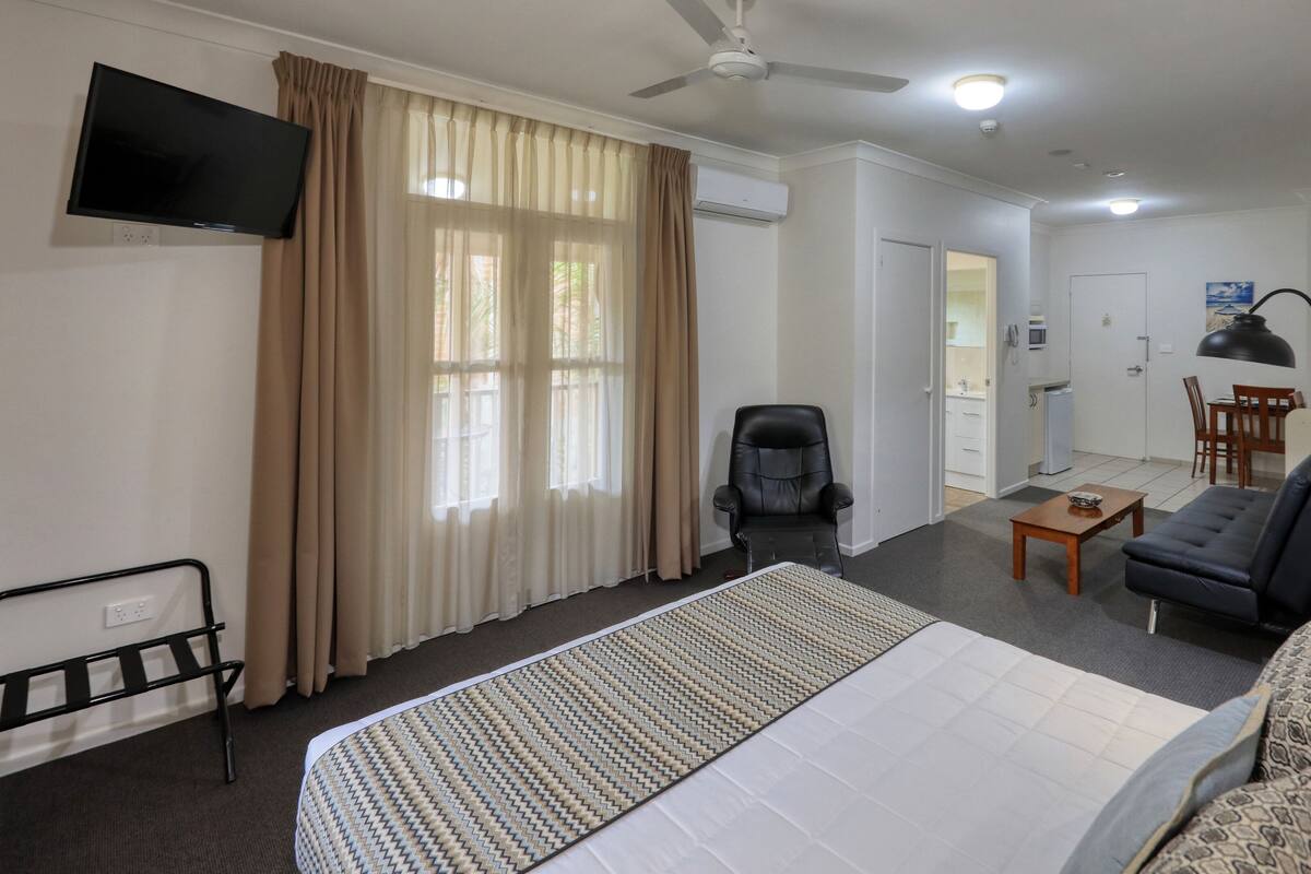 Una habitación de hotel con cama, escritorio, silla, sofá, televisor y ventilador de techo.