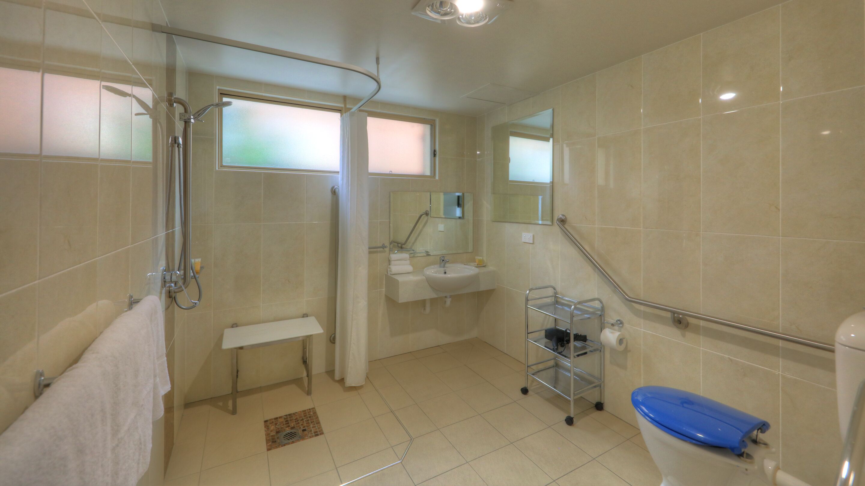 A bathroom with a shower, toilet, sink, and a small bench.