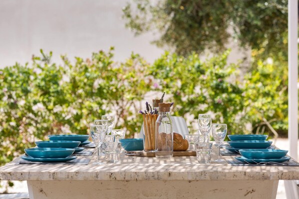Une table dressée à l’extérieur, avec des assiettes bleues, des verres et une bouteille bouchée.