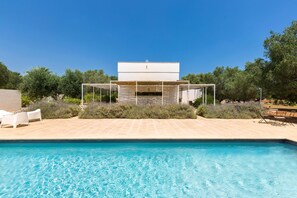 Una piscina con un área de estar exterior moderna y un edificio al fondo.