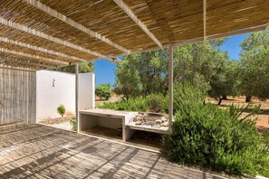 Eine Außenpatio mit einer Holz-Pergola, einer Beton-Sitzgruppe und Blick auf Bäume und Grünflächen.