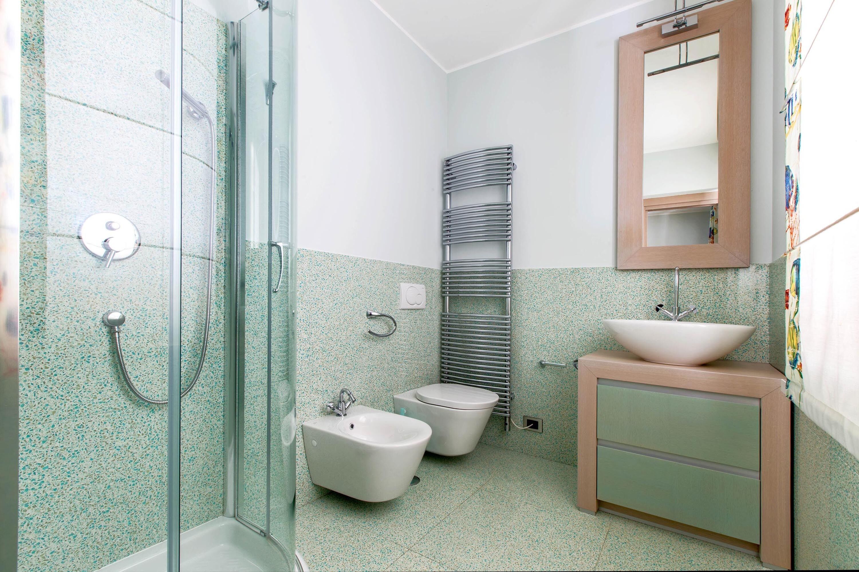 A bathroom with a shower, bidet, toilet, sink, and a mirror.