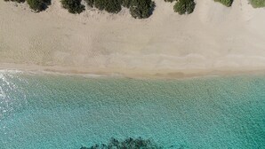 An aerial view of a beach with clear turquoise waters, sandy shore, and dense forest.