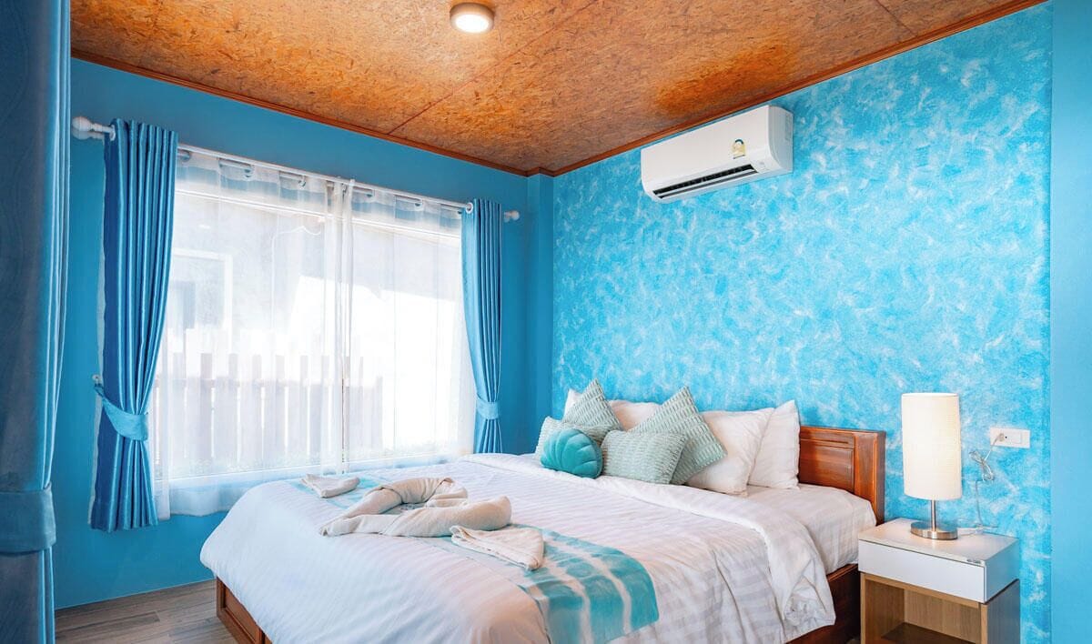 Une chambre avec un plafond en bois, un lit avec une literie blanche, une table de chevet avec une lampe et un climatiseur fixé au mur.