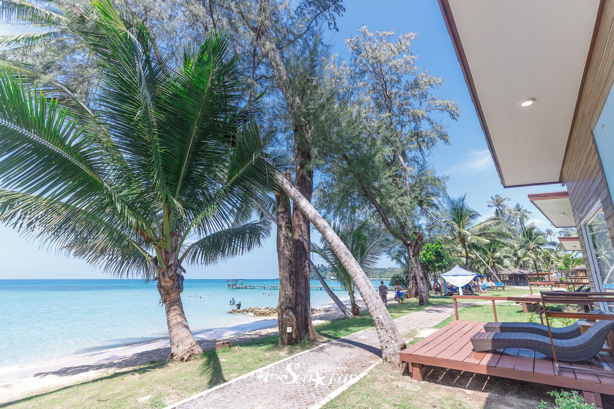 Un resort frente al mar con palmeras, una terraza de madera y vista al océano.