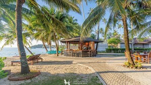 Un área de bar en la playa con una estructura de madera, asientos y vista al mar.