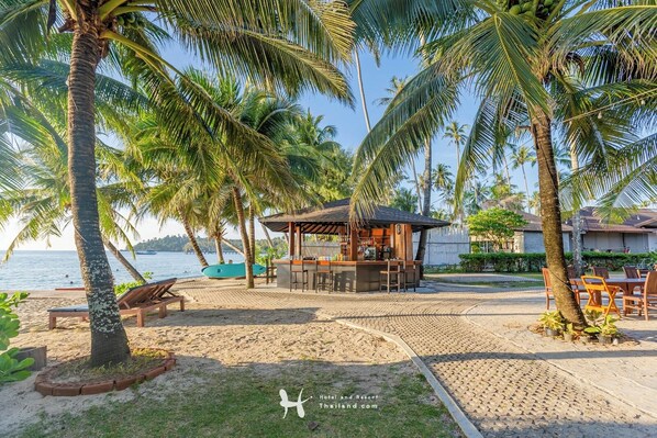 A beachside bar area with a wooden structure, seating, and a view of the sea.