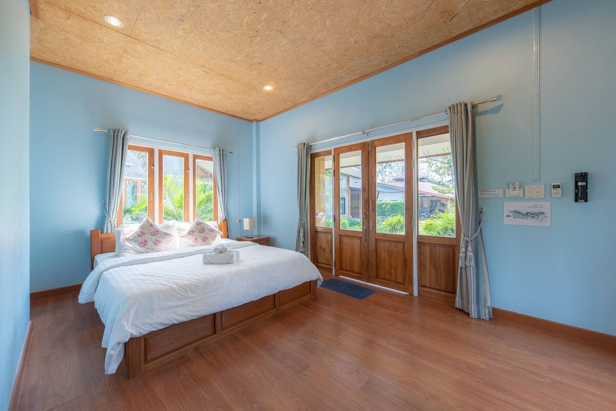 A bedroom with a wooden bed, large windows, and a view of greenery outside.