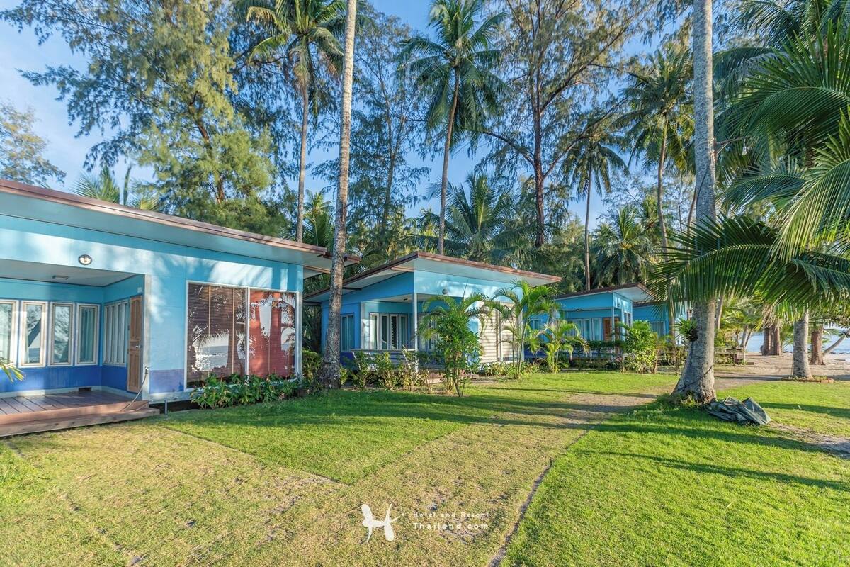 A modern two-story building with a blue exterior, surrounded by lush greenery and palm trees.
