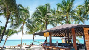 Un bar en la playa con vista al océano, rodeado de palmeras.