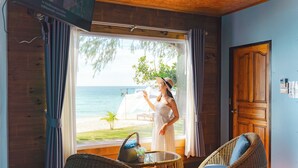 Una habitación con un ventanal grande que da a una playa, muebles de mimbre y una puerta de madera.
