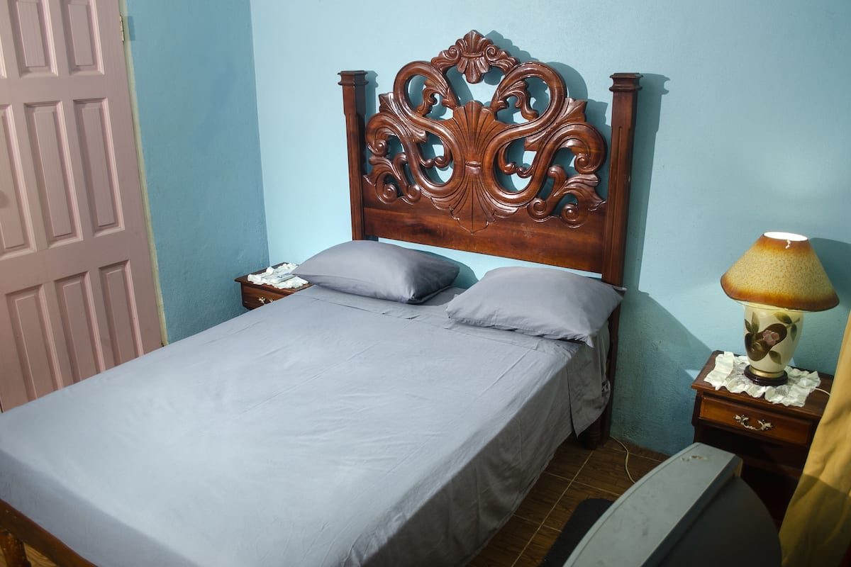 Une chambre à coucher avec une tête de lit en bois, un lit avec des draps gris, une table de chevet avec une lampe et une porte.
