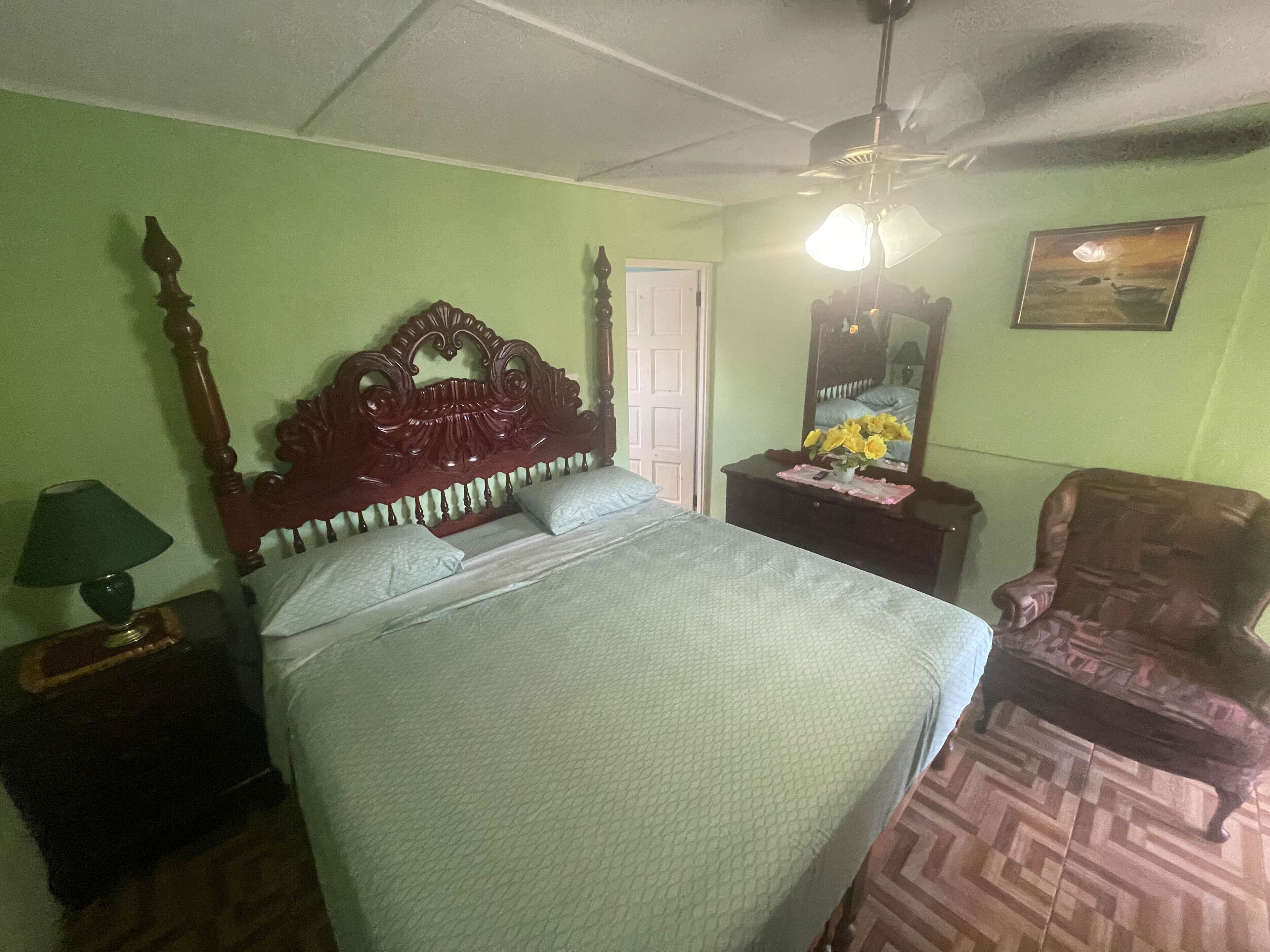 A bedroom with a wooden bed, a nightstand, a chair, a dresser, a ceiling fan, and a mirror.