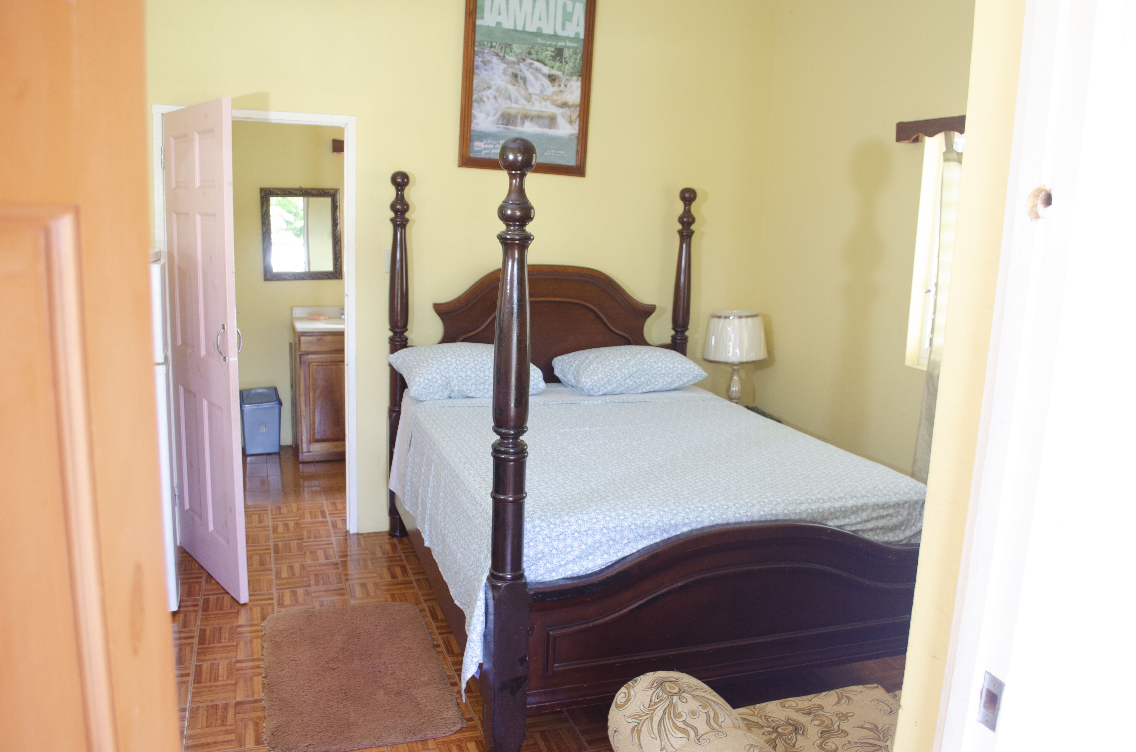 A bedroom with a wooden four-poster bed, a nightstand, a lamp, and a framed picture on the wall.