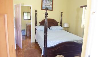 A bedroom with a wooden four-poster bed, a nightstand, a lamp, and a framed picture on the wall.