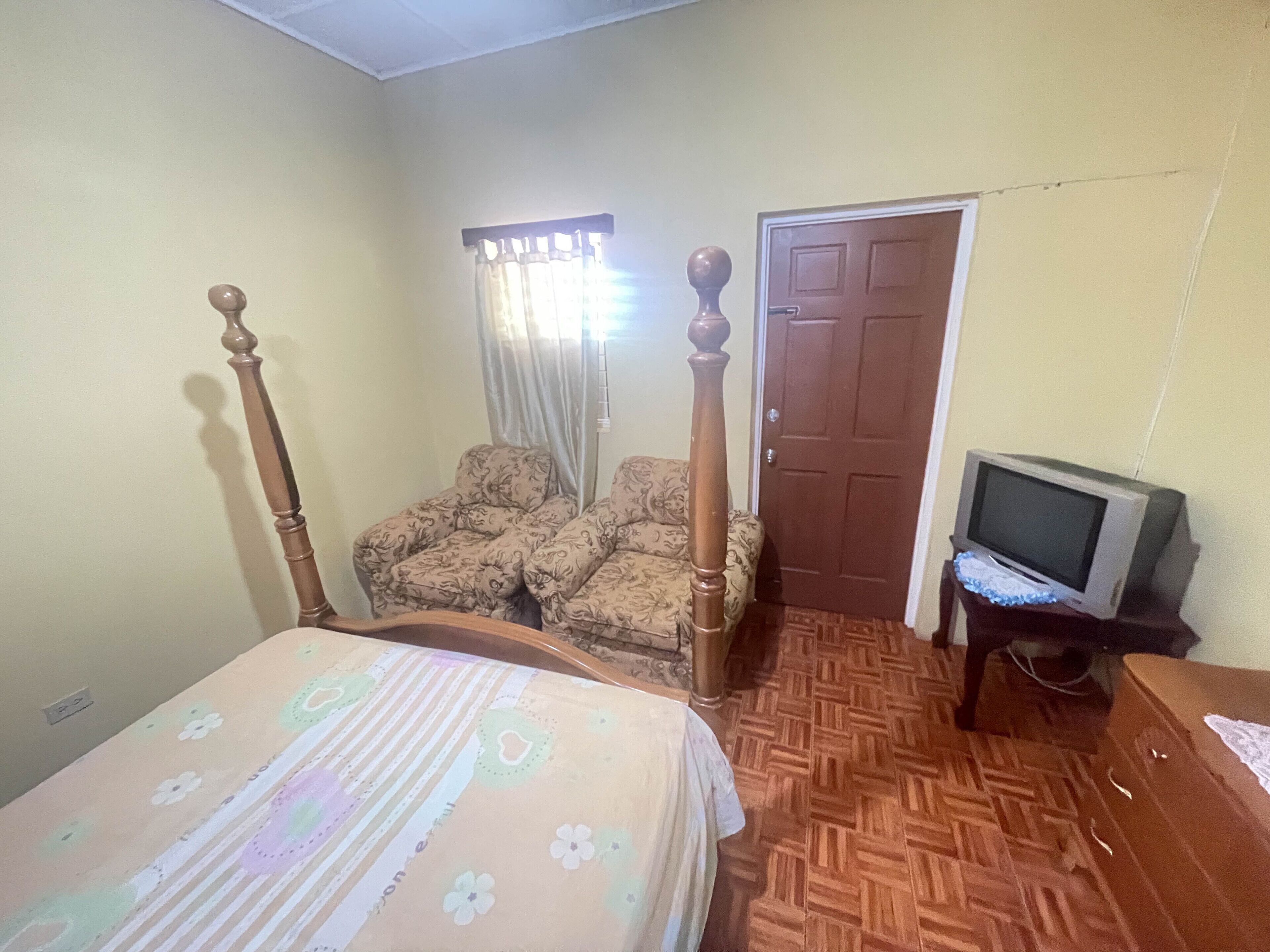 Une chambre à coucher avec un lit à baldaquin, un canapé, un téléviseur posé sur un meuble en bois et une porte.