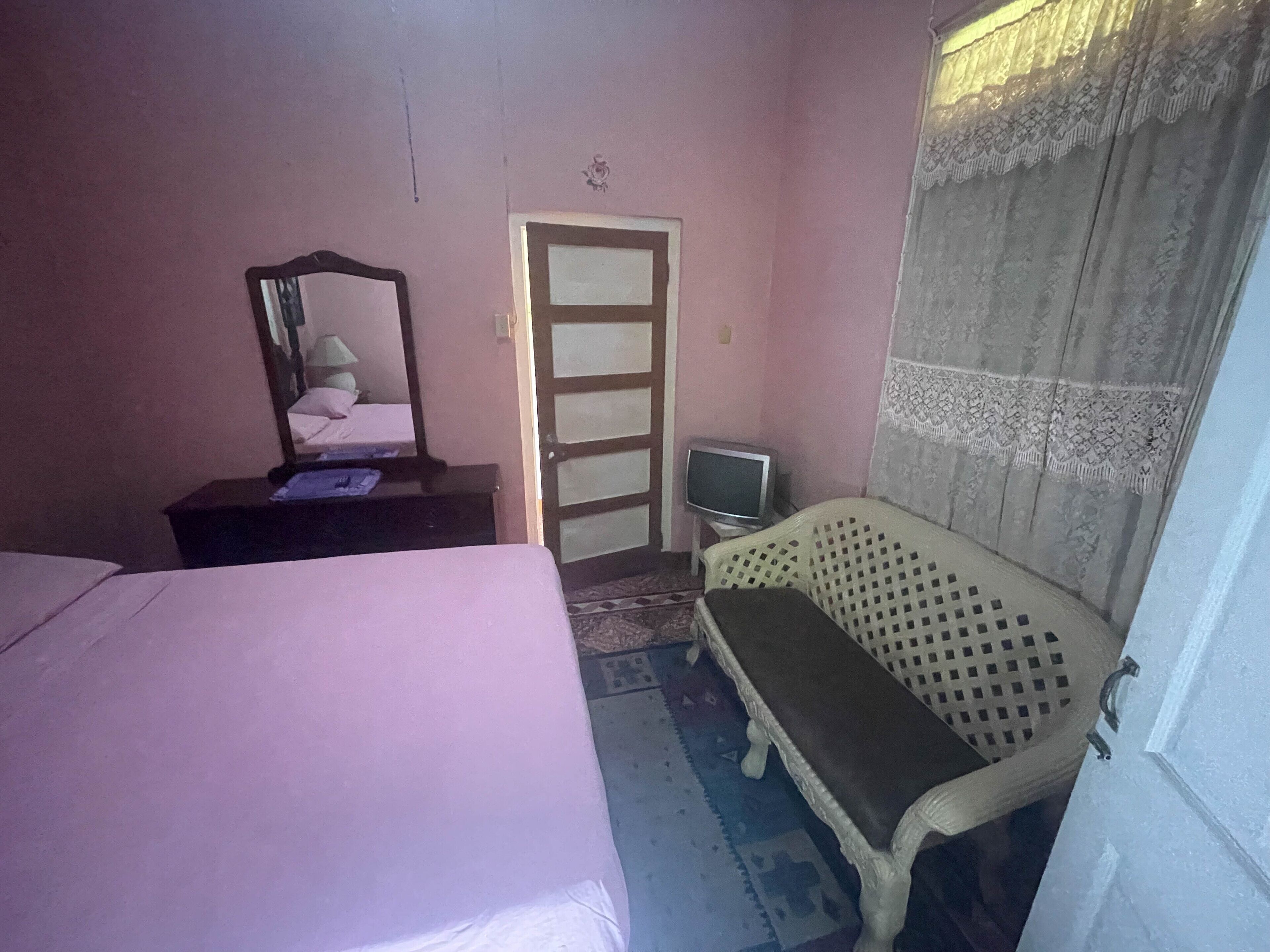 A bedroom with a bed, a bench, a television, and a door.