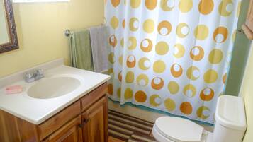 A bathroom with a sink, mirror, toilet, and shower curtain.