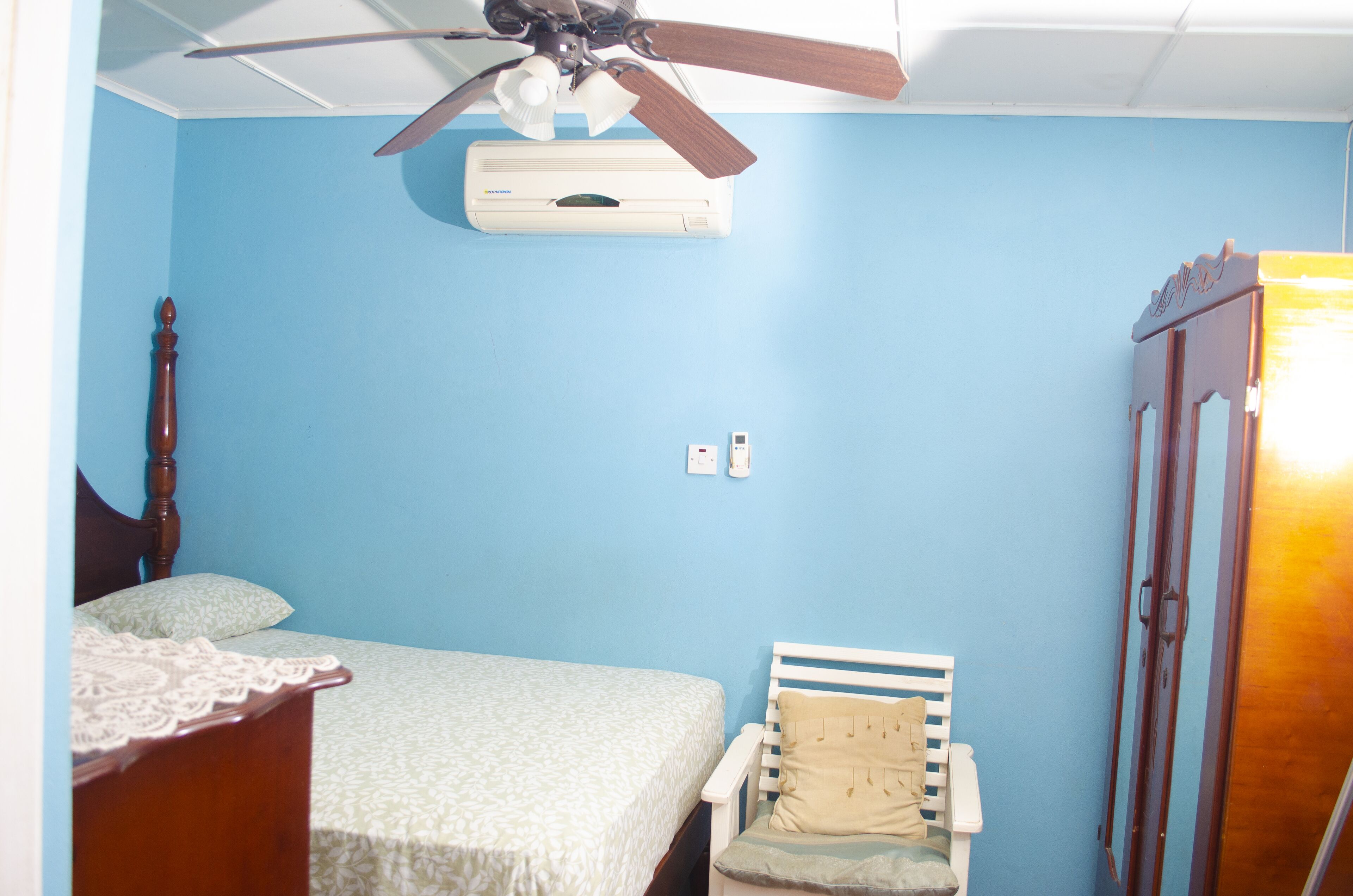 A bedroom with a bed, a chair, a wardrobe, and a ceiling fan.