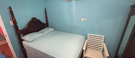 A bedroom with a bed, a chair, a ceiling fan, and an air conditioner.