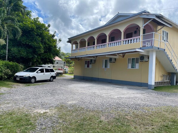 A two-story building with a balcony, a gravel driveway, and a parked white car.