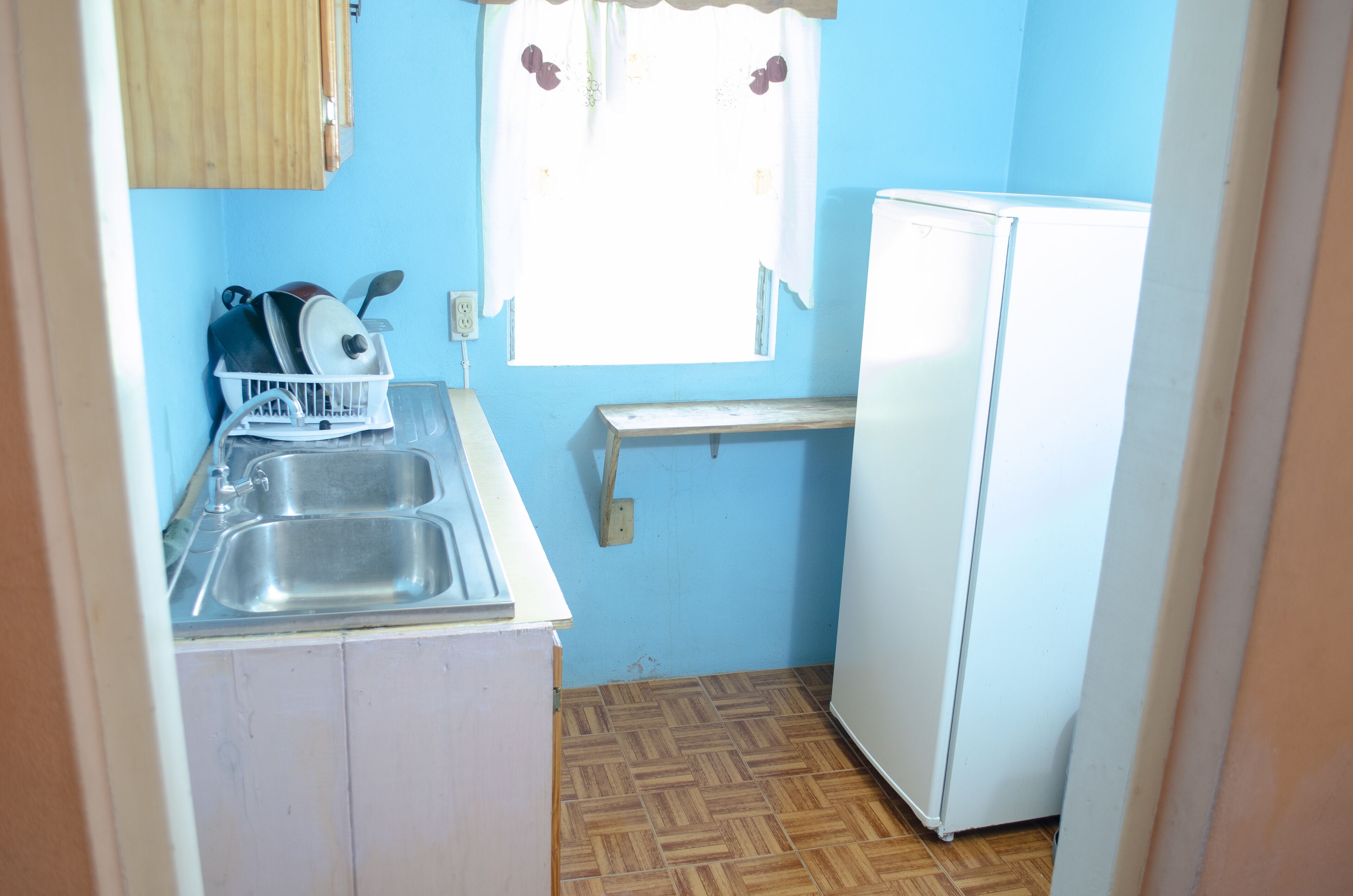 Una cocina compacta con un lavamanos, un refrigerador blanco y una ventana con cortina.