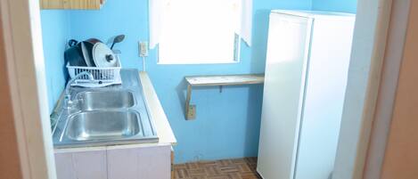 Una cocina compacta con un lavamanos, un refrigerador blanco y una ventana con cortina.