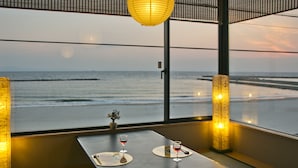 Una habitación con vista al océano, una mesa con un florero y una copa de vino, y una lámpara tradicional.