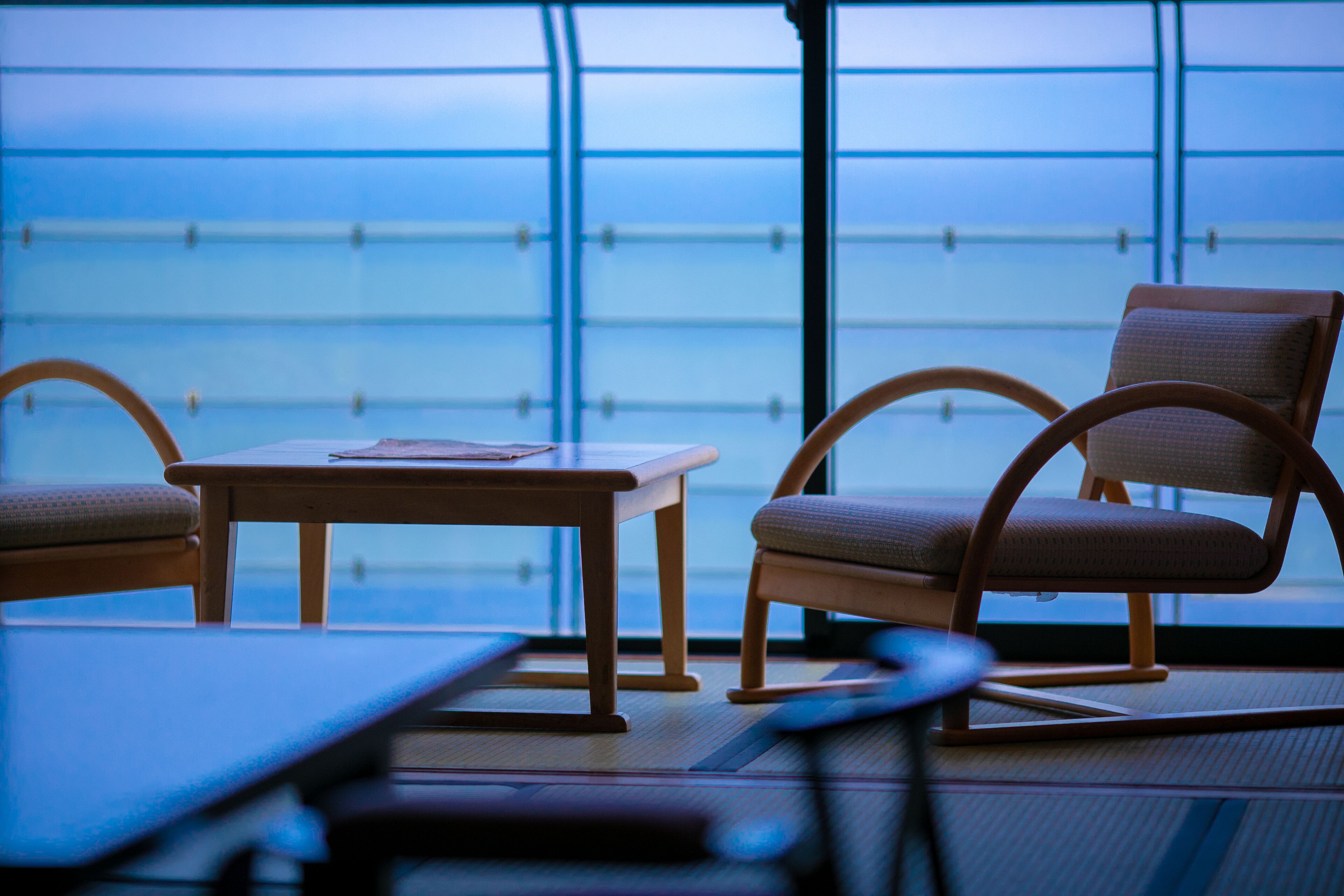 A room with a table and two chairs, a large window with a view, and a floor mat.