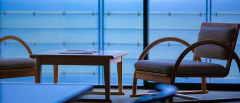 A room with a table and two chairs, a large window with a view, and a floor mat.