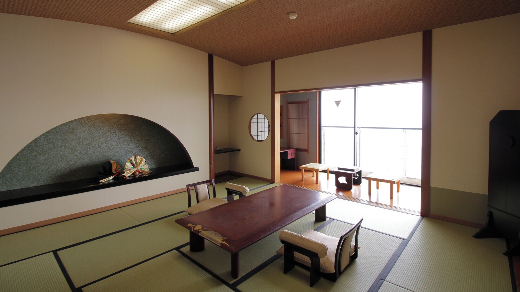 A traditional Japanese room with tatami flooring, a low table, benches, and a sliding door leading to a balcony.