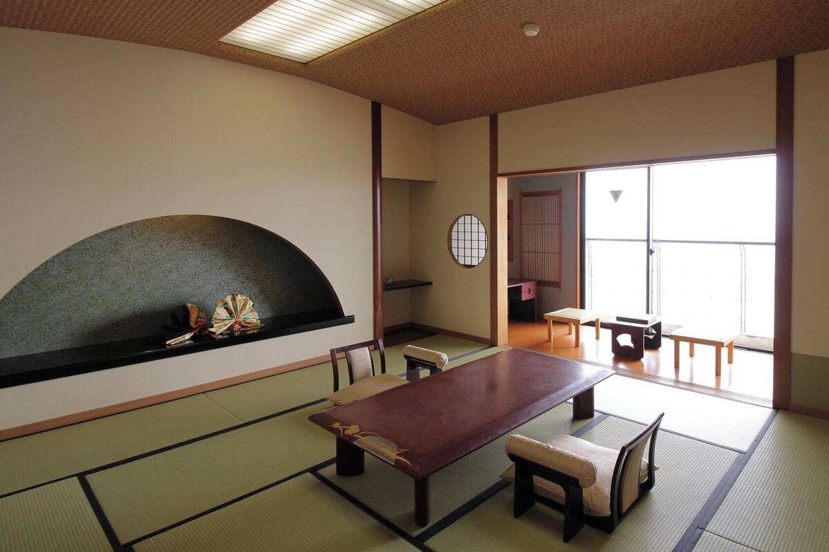 A traditional Japanese room with tatami flooring, a low table, benches, and a sliding door leading to a balcony.