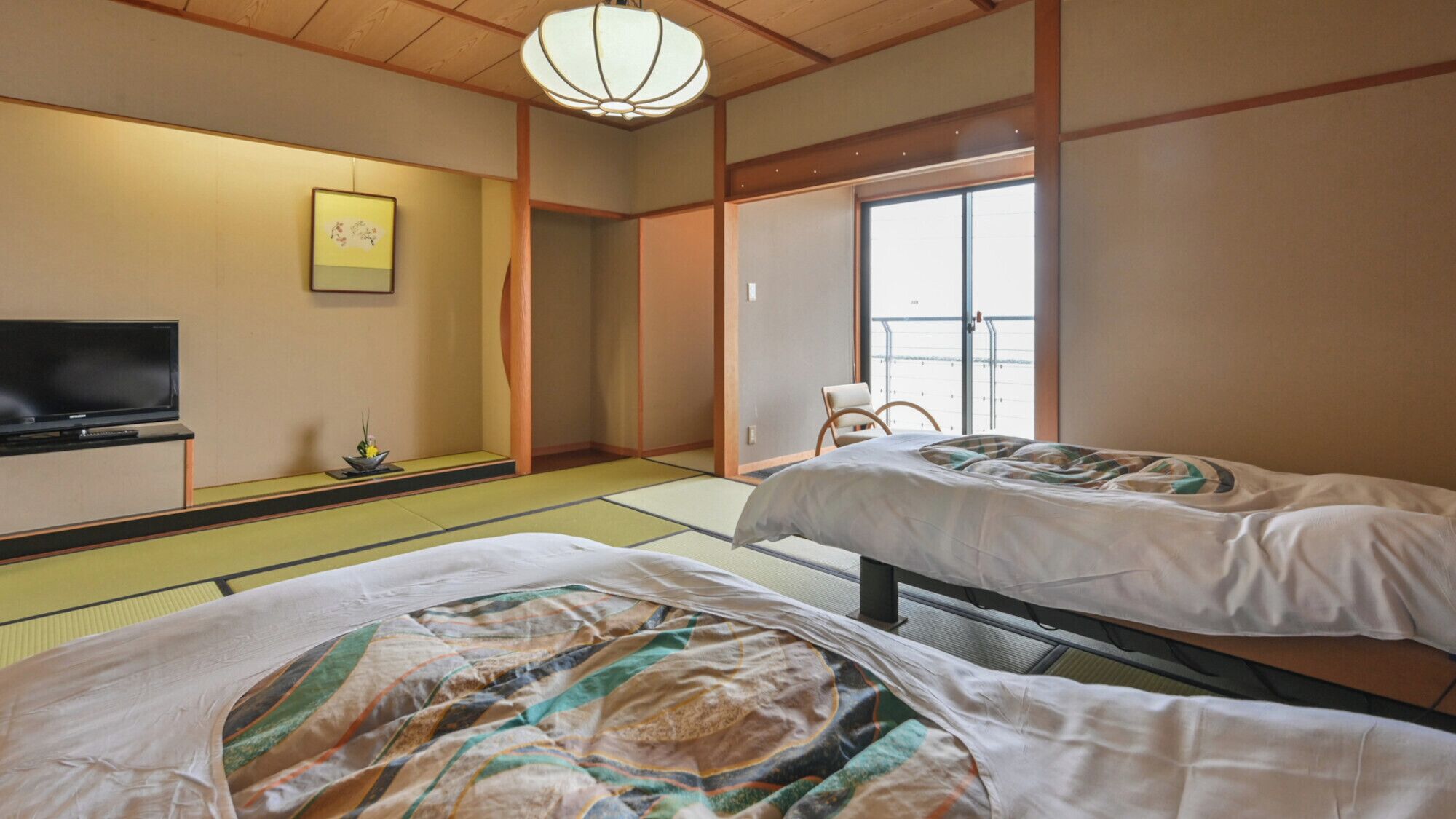A traditional Japanese room with tatami flooring, two beds, a television, and a sliding door leading to a balcony.