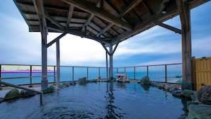 Una terraza de madera con piscina, rodeada de rocas y barandilla, con vista a una masa de agua.