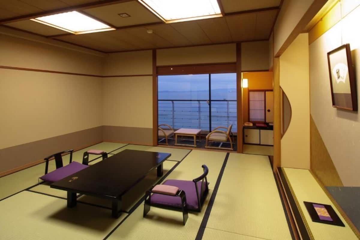A tatami room with a low table and benches, a view of the sea through a sliding door, and a small table with a lamp.