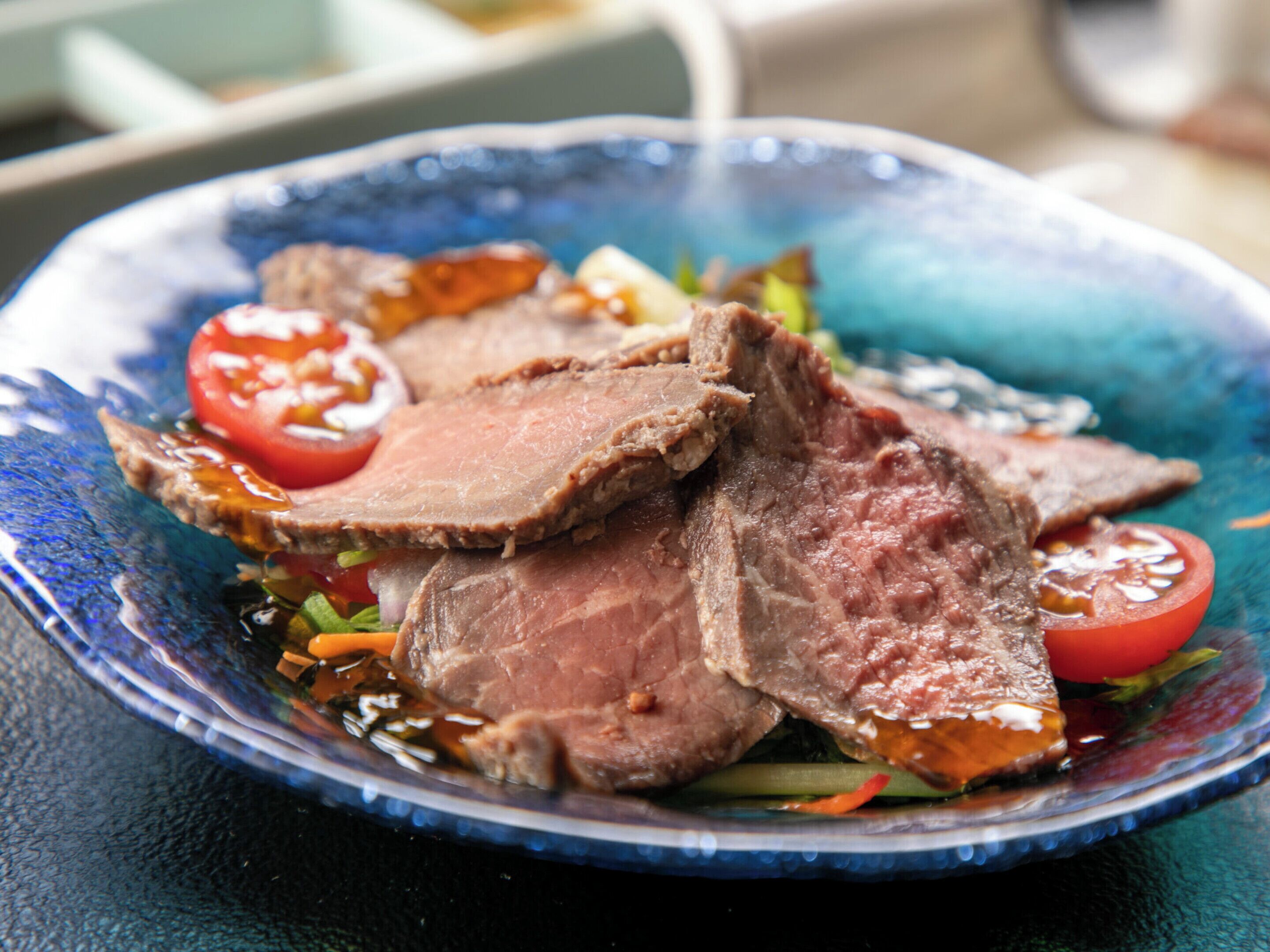 A plate of sliced beef with vegetables.