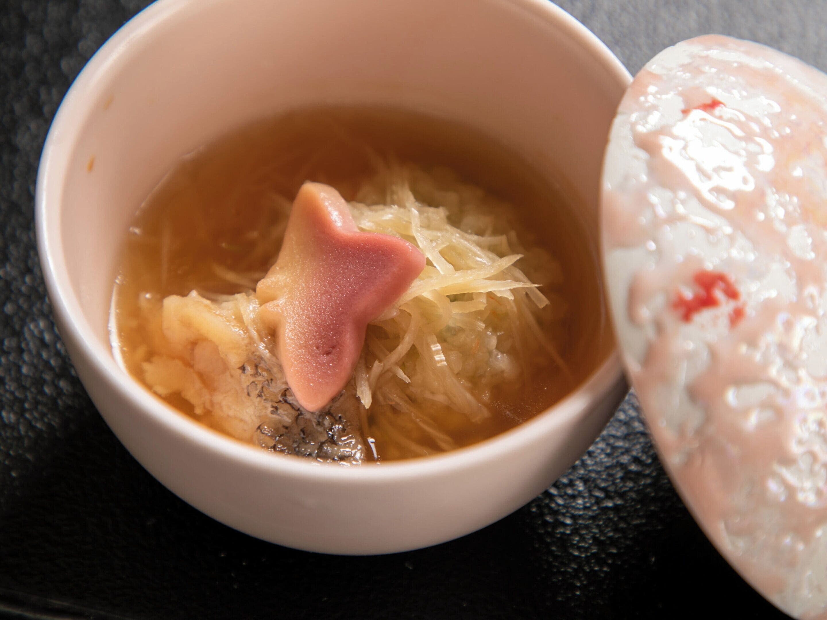A bowl of soup with a heart-shaped garnish and a dumpling on the side.
